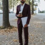 Man in suit holding coffee and document on a leaf-covered street during autumn.